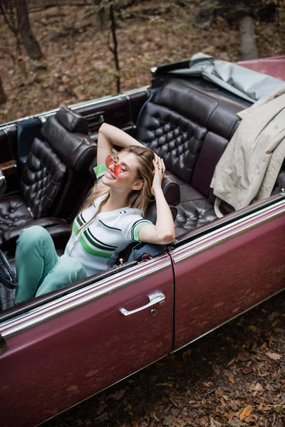 Cabriolet 'te elleri ve gözleri kapalı oturan neşeli kadının yüksek açılı görüntüsü.