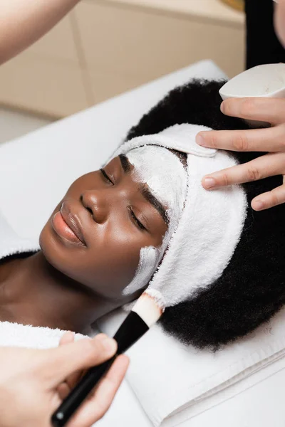 非洲裔美籍妇女在温泉沙龙面罩上涂化妆品刷的温泉治疗师近景 — 图库照片