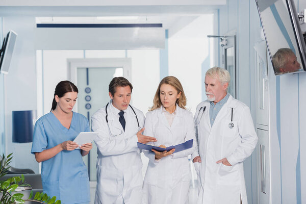 Селективный акцент врача, указывающего на коллег с цифровыми планшетами и планшетами в клинике 