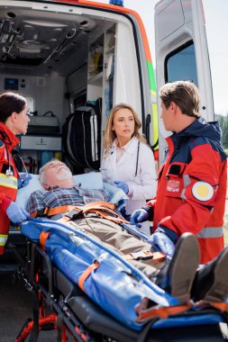 Selective focus of doctor looking at paramedic near patient on stretcher and ambulance car  clipart