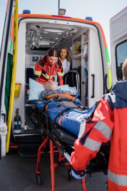 Selective focus of paramedics holding stretcher with senior patient near ambulance car  clipart