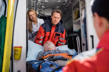 Ambulans arabasında dijital tabletli bir doktorun yanında hastayı sedyede tutan sağlık görevlilerinin seçici odağı 