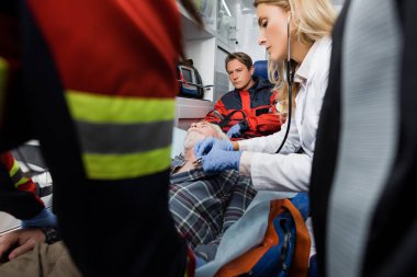 Doktorun yanında durup, ambulans arabasında steteskopla hastayı inceleyen sağlık görevlilerinin seçici odağı. 