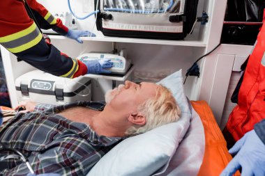 Ambulans arabasında lateks eldivenli, sağlık görevlilerinin yanında yatan yaşlı bir hastanın seçici odağı. 