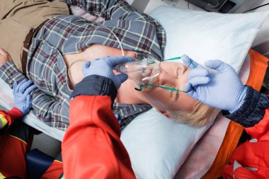 Ambulans arabasındaki hasta hastaya oksijen maskesi takan lateks eldivenli sağlıkçının seçici odağı. 