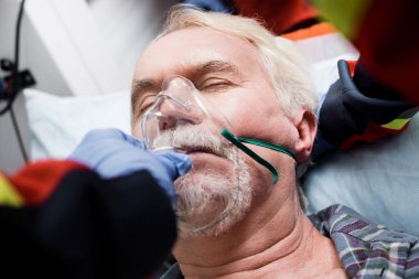 Selective focus of paramedic wearing oxygen mask on ill patient during first aid  clipart