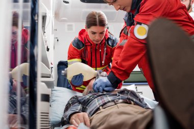 Selective focus of paramedics in uniform doing cardiopulmonary resuscitation to man during first aid  clipart