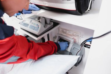Cropped view of paramedic in latex gloves using equipment in ambulance car  clipart