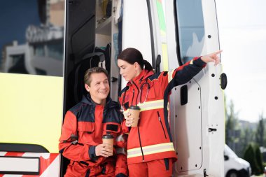 Paramedikler, tek kullanımlık bardağı iş arkadaşı ve ambulans arabasının yanında tutarken parmağı ile işaret ediyorlar. 