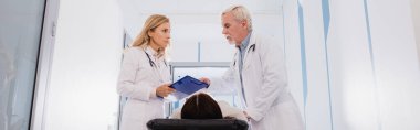 Stetoskoplu ve dosyalı doktorların internet sitesi başlığı klinikte sedyede hasta bir kadının yanında duruyor. 