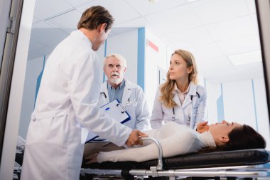 Doktorların seçici odak noktası klinik koridorundaki sedyeyi kapatan hasta yakınındaki dosyasına bakması. 