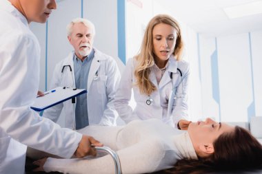 Elinde dosya olan doktorların seçici odak noktası klinik koridorundaki sedyeye kapalı bakan kadınlara bakmak. 