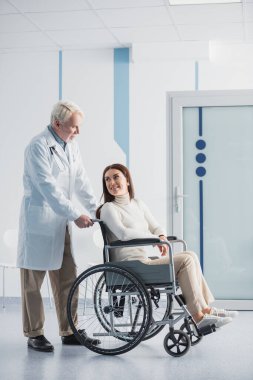 Klinikte kıdemli doktorun yanında tekerlekli sandalyede oturan engelli hasta. 