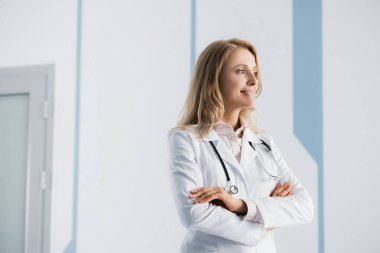 Sarışın doktor kollarını kavuşturup kliniğe bakıyor. 