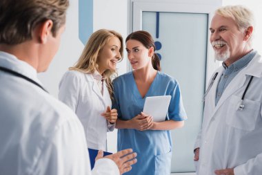 Doktorun klinikteki meslektaşlarının yanında dijital tabletli hemşireyle konuşması seçici bir odak noktası. 