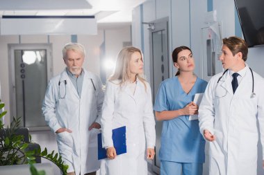 Hastanedeki meslektaşlarının yanında elinde dosya ve dijital tabletle yürürken doktorların seçici odak noktası 