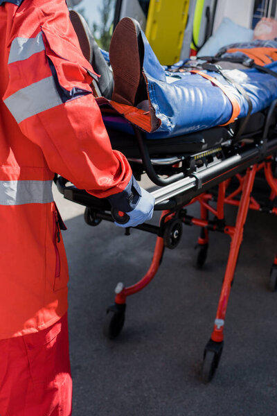 Selective focus of paramedic holding stretcher with senior patient near ambulance car 