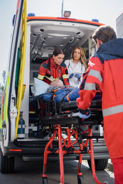 Selective focus of paramedic carrying stretcher with patient near doctor with digital tablet in ambulance car 