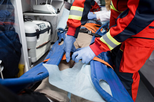Обрезанный вид парамедиков, держащих ремни носилок рядом с пациентом в машине скорой помощи 