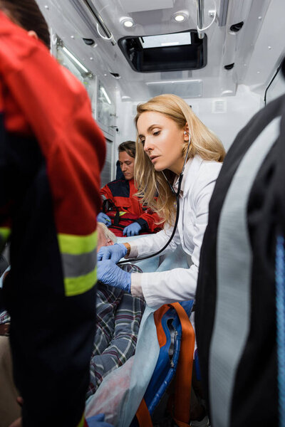 Selective focus of doctor examining patient with stethoscope near paramedics in ambulance car 