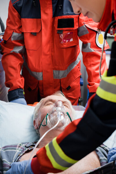 Selective focus of paramedic standing near patient in oxygen mask during first aid 