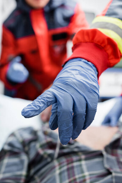 Selective focus of paramedic in latex glove pointing with finger near patient and colleague 