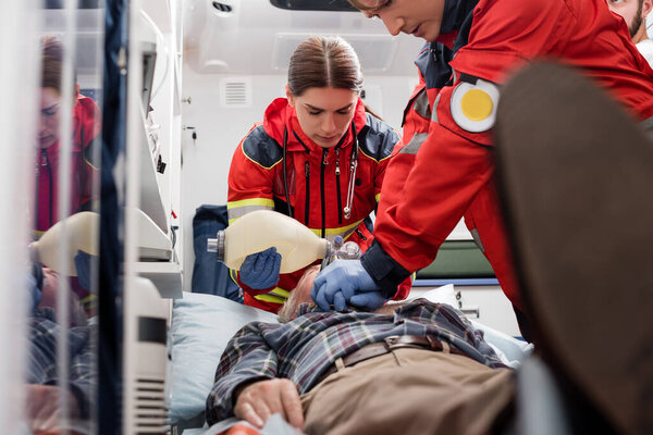 Selective focus of paramedics in uniform doing cardiopulmonary resuscitation to man during first aid 