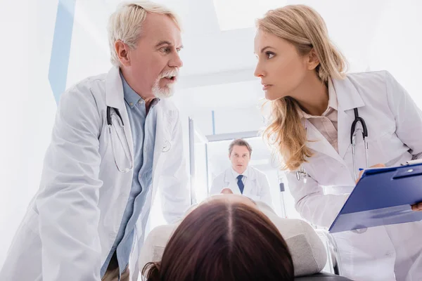 Selective Focus Senior Doctor Talking Colleague Clipboard Patient Stretcher Clinic — Stock Photo, Image