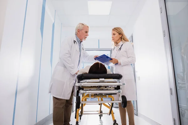 Doctor Holding Clipboard Senior Colleague Sick Patient Stretcher Clinic — Stock Photo, Image