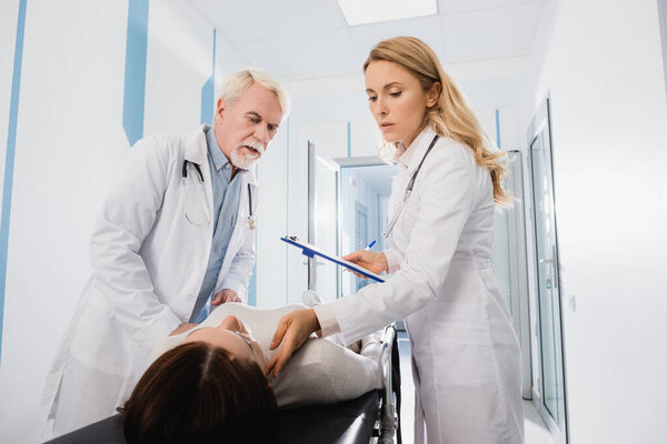 Селективный фокус врача с планшетом проверки пульса пациента на носилках рядом с коллегой в клинике 