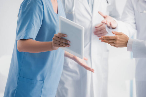 Обрезанный вид медсестры, показывающей цифровые таблетки рядом с врачами в клинике 