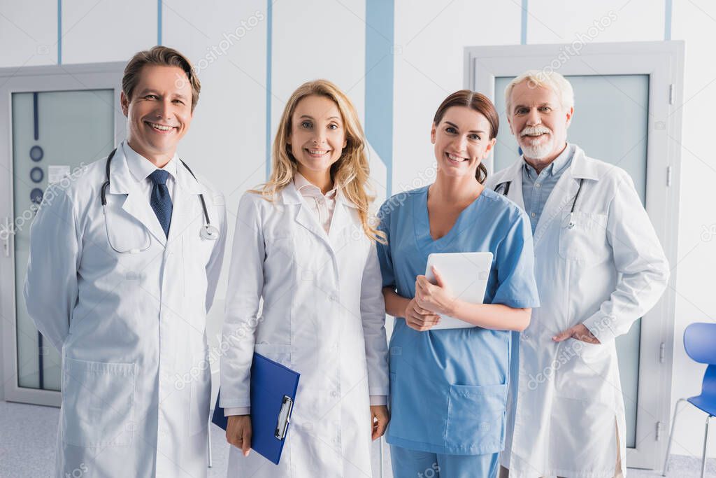 Hospital staff with digital tablet and clipboard looking at camera in clinic