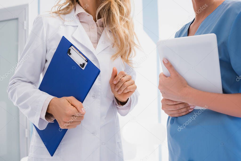 Cropped view of doctor holding clipboard near nurse with digital tablet in clinic 