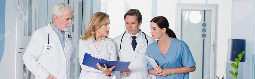 Horizontal crop of doctor showing clipboard to colleagues and nurse 