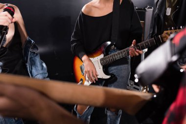 KYIV, UKRAINE - AUGUST 25, 2020: Cropped view of woman with electric guitar standing near female vocalist with microphone on blurred foreground clipart