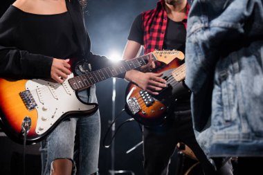 KYIV, UKRAINE - AUGUST 25, 2020: Cropped view of rock band musicians playing electric guitars with blurred jeans jacket on foreground clipart