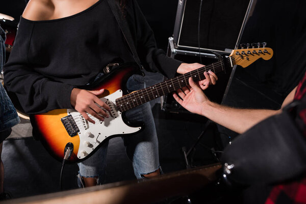 KYIV, UKRAINE - AUGUST 25, 2020: Cropped view of man touching guitar strings, while woman playing during rock band rehearsal