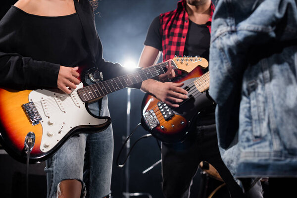 KYIV, UKRAINE - AUGUST 25, 2020: Cropped view of rock band musicians playing electric guitars with blurred jeans jacket on foreground