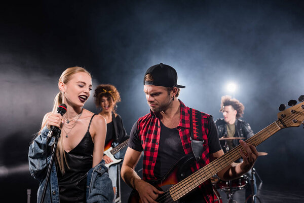 KYIV, UKRAINE - AUGUST 25, 2020: Smiling blonde woman singing near guitarist during rock band rehearsal with backlit on blurred background