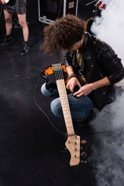 KYIV, UKRAINE - 25 AĞUSTOS 2020: Rock grubu provası sırasında elektro gitarıyla çömelmiş kıvırcık müzisyen manzarası