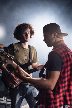 KYIV, UKRAINE - 25 AĞUSTOS 2020: Kıvırcık rock grubu müzisyeni ayakta duruyor ve arka planda dumanı olan elektro gitaristin elektro gitaristine bakıyor