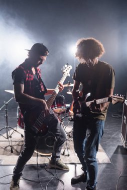 KYIV, UKRAINE - 25 Ağustos 2020: Rock grubu müzisyenleri arka planda arka plan ışığı olan davul setinin yanında elektro gitar çalıyorlar