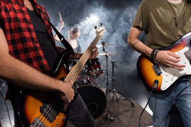 KYIV, UKRAINE - AUGUST 25, 2020: Musicians playing electric guitars with smoke and blurred female drummer on background clipart