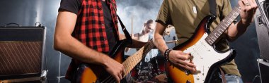 KYIV, UKRAINE - AUGUST 25, 2020: Rock band musicians playing bass guitars with smoke and blurred female drummer on background, banner clipart
