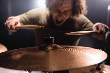 Metal cymbal with blurred drummer holding drumsticks background clipart