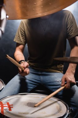 Obscure face of musician with drumsticks playing drum on black clipart