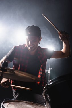 Rock grubu davulcusu bageti tutuyor ve arka planda ışık ve dumanla davul çalıyor.