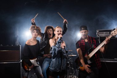 KYIV, UKRAINE - 25 AĞUSTOS 2020: Rock grubu müzisyenleri siyah arka ışıklandırmalı müzik enstrümanları tutarken bağırıyor