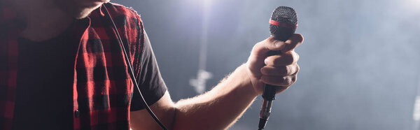 Cropped view of vocalist of rock band holding microphone on blurred background, banner
