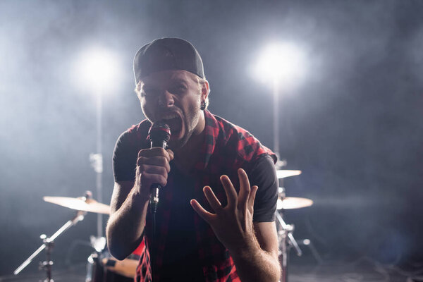 Rock band vocalist screaming while holding microphone on blurred background